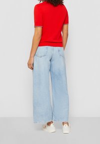 Czerwona bluzka z krótkim rękawem w białe wykończenie, zestawiona z jasnoniebieskimi spodniami typu wide-leg. Strój uzupełniają białe trampki z subtelnymi detalami.