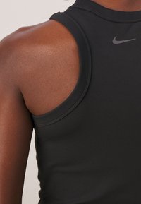 Czarny sportowy tank top wykonany z gładkiego materiału, z okrągłym dekoltem, bez rękawów oraz małym szarym logo Nike na piersi.
