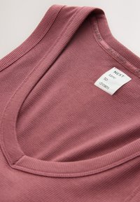 T-shirt mauve côtelé doux à col en V avec une étiquette blanche mentionnant « NEXT time to dream » près de l'encolure.