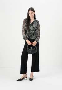 Blusa trasparente a maniche lunghe con stampa floreale nera e scollatura a V, abbinata a pantaloni neri a vita alta e gamba larga e una piccola borsa nera.