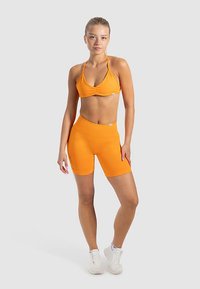 Oranges sportliches Bustier und hoch tailliertes Shorts-Set. Dehnbarer Stoff, schlankes Design, mit gerafftem Vorderdetail und glatter Textur.