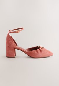 Chaussure en daim rose à talon moyen avec bride à la cheville, boucle dorée, bout arrondi et détails froncés à l'avant.