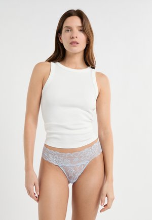 Weißes geripptes Tanktop kombiniert mit einem hellblauen Spitzen-String mit Blumenmuster und gewelltem Rand.