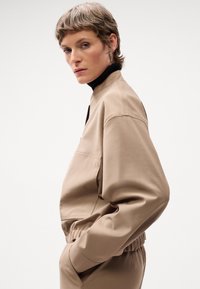 Beige kort jacka i slätt tyg, med dragkedjestängning, hög krage och korta ärmar med en avslappnad passform.