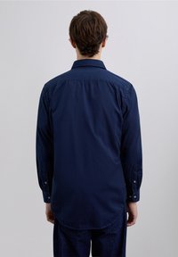 Camisa azul marino de algodón suave con botones, que presenta un cuello clásico, mangas largas y un dobladillo curvado en la parte trasera.