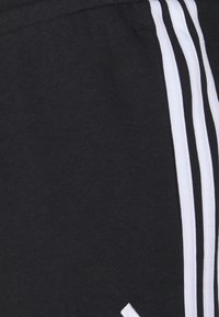 Pantalones cortos deportivos negros de algodón, con rayas verticales blancas en los laterales y una textura suave. Sin herrajes visibles ni patrones.