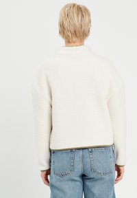 Cremefarbener Fleece-Jacke mit lockerer Passform, hohem Kragen und überschnittenen Schultern. Sie hat eine weiche Textur und einen kontrastierenden Saum mit einer Naht.