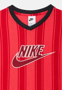 Κόκκινη αθλητική φανέλα Nike με μαύρο γιακά και κατακόρυφες ρίγες, με μεγάλο λογότυπο Nike και swoosh στο κέντρο.