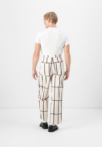 T-shirt bianco a maniche corte abbinato a pantaloni crema con un motivo a quadri marrone. I pantaloni hanno un vita alta e gamba larga.