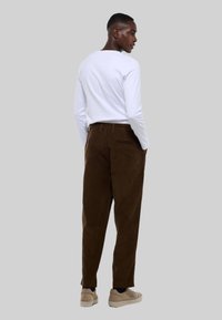 Pantalon en velours côtelé marron à coupe droite avec deux poches arrière, associé à une chemise blanche à manches longues et des chaussures slip-on beiges.