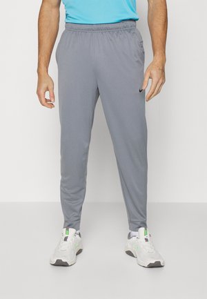 Hombre vestido con pantalones deportivos grises de Nike y zapatillas blancas, de pie contra un fondo blanco liso.