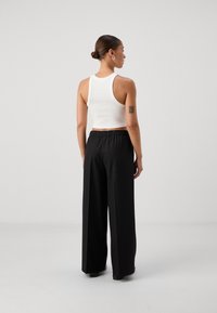 White cropped tank top with a round neckline and sleeveless design paired with black wide-leg trousers featuring an elastic waistband.