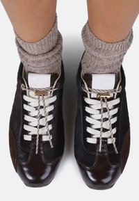 Black and brown athletic shoes featuring glossy leather and textured fur, white laces, and metallic hardware accents.