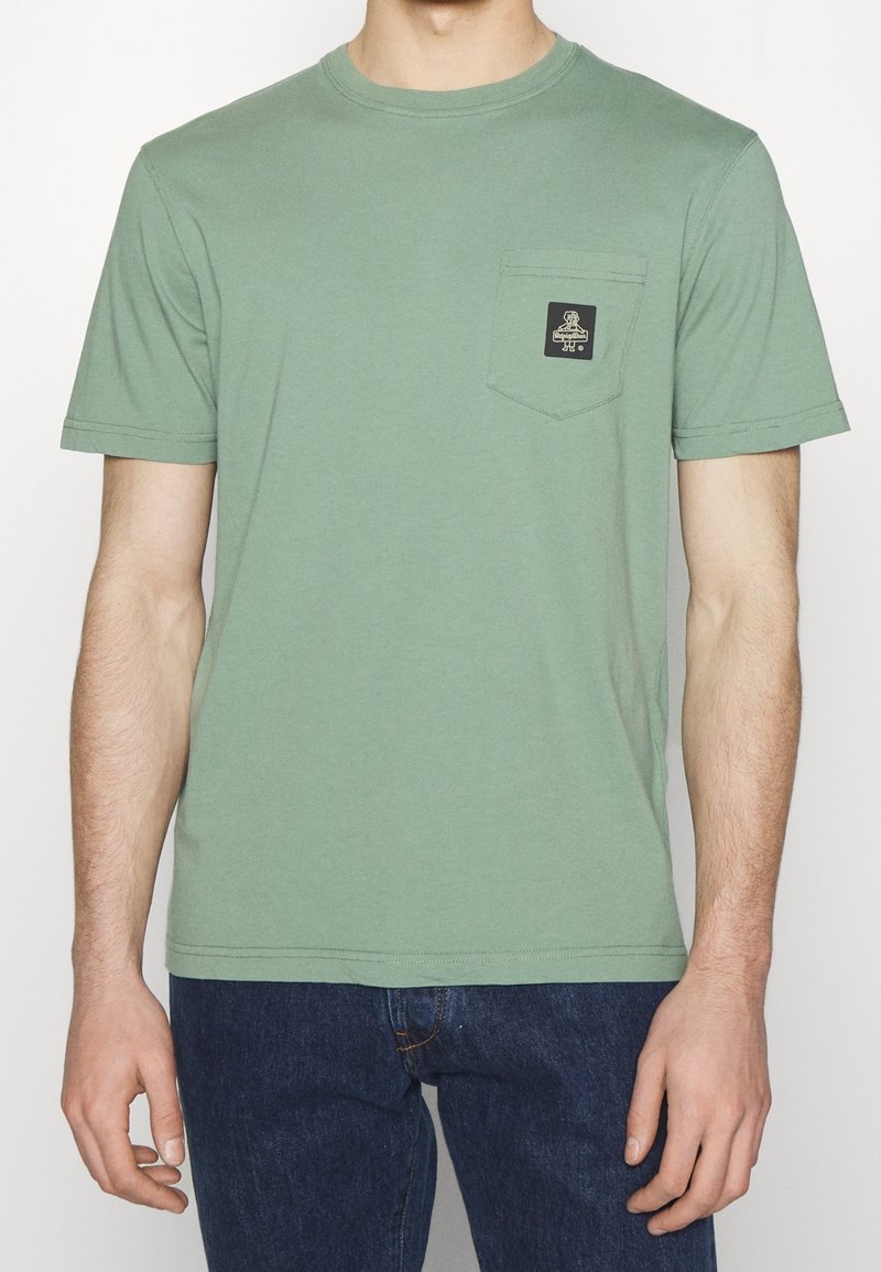 Kortärmad t-shirt med rund halsringning i dämpad grön bomull, med en bröstficka som har en svart logotyp-badge. Liten, rak fåll.