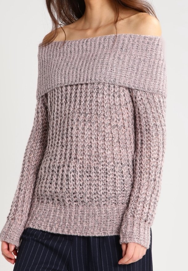 Femme portant un pull en maille grosse et violet clair, à épaules dénudées et manches longues, avec un pantalon à rayures fines bleu marine.