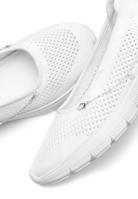 Weiße Slipschuhe mit einem atmungsaktiven Mesh-Obermaterial, strukturierter Oberfläche und einem silbernen Kettenakzent. Verfügt über eine flexible Gummisohle.