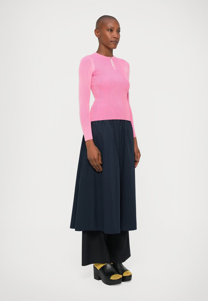 Fitted pink ribbed sweater with long sleeves, paired with a flowing dark navy skirt. Black platform shoes with yellow accents.