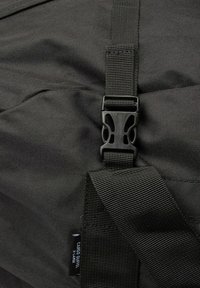 Musta kangaskassi, jossa on teksturoitu pinta, varustettuna muovikiinnityksellä ja tukevilla webbihihnoilla. Tunnisteessa lukee "Cargo Duffel X-Large."