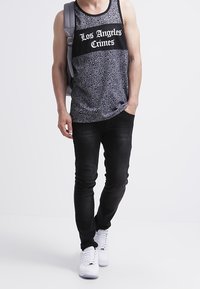 Top negro sin mangas con un patrón de paisley, panel de malla contrastante con el texto "Los Angeles Crimes". Combinado con jeans oscuros y zapatillas blancas.