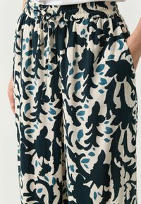 Loose-fitting pants with an elastic waistband, featuring a navy and teal floral pattern on a cream background. Includes side pockets.