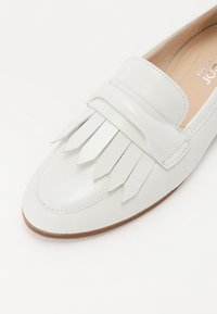 White leather loafer featuring a fringing detail on the upper, stitched accents, and a smooth finish, with a rounded toe and flat sole.