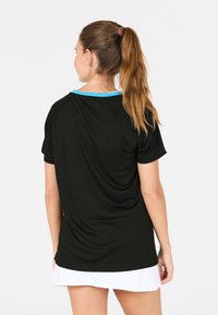 Svart sporttröja med korta ärmar, en blå krage och en slät textur, delvis instoppad i en vit kjol, sedd bakifrån.