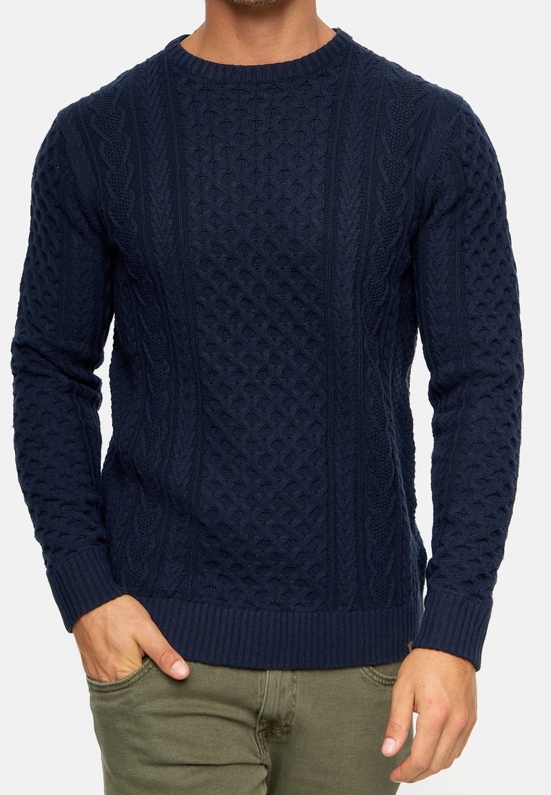 Navy knitted sweater with intricate cable and diamond patterns, round neck, and ribbed cuffs and hem, made from soft, textured fabric.