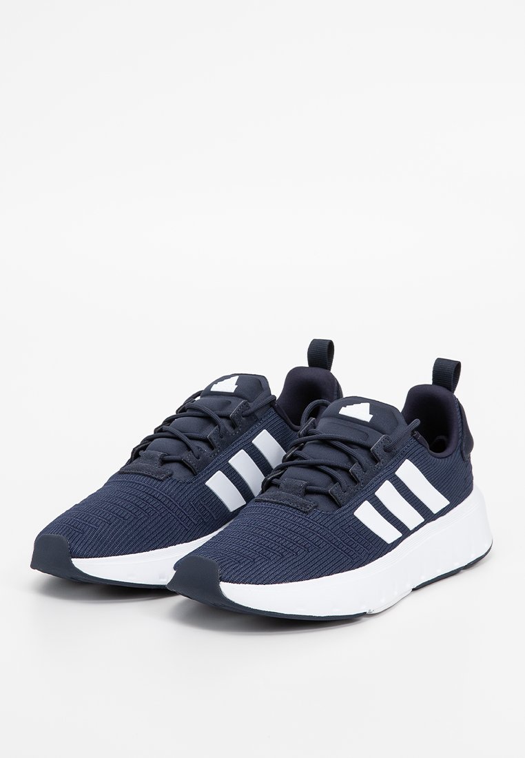 Marineblaue Sportschuhe mit einem strukturierten Strick-Obermaterial und drei weißen Streifen an der Seite. Ausgestattet mit Schnürsenkeln und einer gepolsterten weißen Sohle.