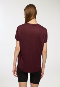 Bordowa koszulka z krótkim rękawem, okrągłym dekoltem, gładką teksturą i lekko wydłużonym tylnym hemem. Połączona z czarnymi szortami.