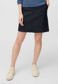 Une jupe en coton bleu marine foncé avec une coupe droite, présentant une texture lisse et un design minimaliste, accompagnée de chaussures beiges à lacets.