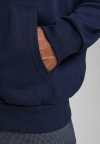 Marineblaue Sweatshirt aus Baumwollmischung, mit gerippten Bündchen und Saum, und einer Seitentasche, die teilweise von einer Hand gefüllt ist.