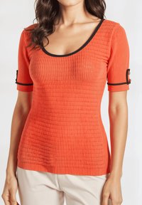 Top ajustado de canalé en naranja brillante con escote redondo y ribete negro; las mangas cortas presentan un detalle de dos botones en los puños.