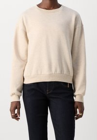 Sudadera beige con cuello redondo, textura suave, hombros caídos y dobladillo acanalado. Combinada con jeans azul oscuro.
