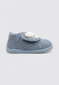 Pantoufle bleue en peluche, faite d'un matériau texturé, dotée d'un patch rond avec un motif de mouton blanc et une sangle grise. Semelle en caoutchouc flexible.