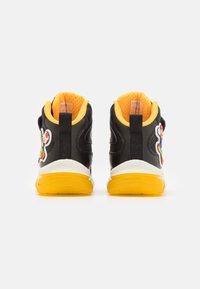 Zapatillas altas con un exterior de tela negra, acentos en amarillo brillante, una suela blanca y parches decorativos de personajes en el lateral.