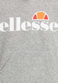 Szary sweatshirt z dużym białym logo "ellesse" oraz pomarańczowym i czerwonym akcentem w kształcie półkola. Posiada przednią kieszeń kangurkę i miękką fakturę.