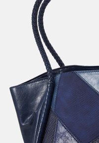 Marinblå läder tote-väska med texturerad lapptäckesdesign, med flätade handtag och varierande ytbehandlingar i mörkblå nyanser.