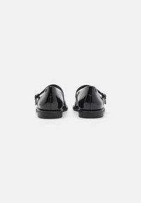 Black patent leather shoes with a smooth finish, rear view showing a rounded heel and decorative side accents.