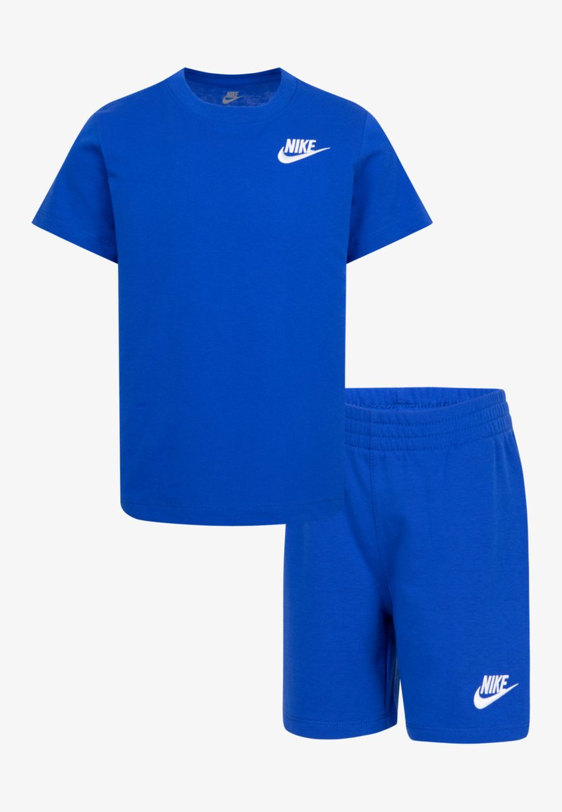 Mėlynas medvilnės marškinėlių ir šortų komplektas. Marškiniai su apvaliu kaklu ir trumpomis rankovėmis; abu drabužiai turi baltą „Nike“ logotipą. Šortai turi elastinę juostą.
