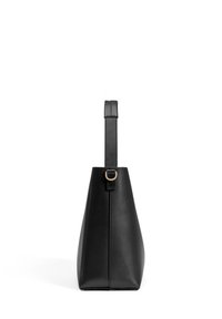 Black leather handbag with a tapered design. Smooth texture, flat base, and a single adjustable strap with a gold accent near the top.