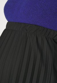 Gonna nera a pieghe con vita elastica, abbinata a un top viola con texture, che mette in risalto colori a contrasto e diverse trame di tessuto.