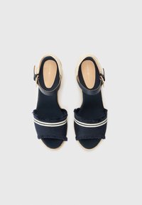 Námořnické espadrilky s roztrhaným textilním svrškem, elastickými pruhovanými detaily a zapínáním na přezku. Klínový podpatek obalený jutou. Rovná podešev.