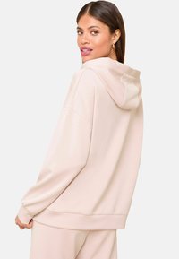 Kerge roosa kapuutsiga sviiter, millel on mugav lõike, kootud varrukaotsad ja nööriga kapuuts. Pehme tekstuur ja minimalistlik disain.