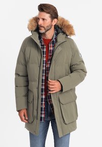 Grüne gepolsterte Parka mit einer fellgefütterten Kapuze, ausgestattet mit mehreren Taschen, einem Reißverschluss und einem karierten Hemd darunter.