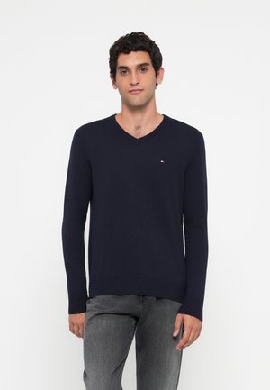 Marineblauer V-Ausschnitt-Pullover aus weichem Baumwollmaterial, mit langen Ärmeln und einem kleinen Logo-Akzent auf der Brust, tailliert geschnitten.
