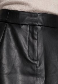 Falda de cuero negro con textura suave, con una cinturilla plana y un bolsillo lateral. Detalle de costura visible a lo largo de la costura.
