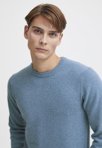 Light blue sweater made from soft material, featuring a crew neckline and ribbed cuffs. The fabric appears textured with a slightly fuzzy finish.