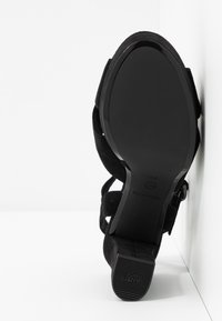 Sorte suede hælede sandaler med et struktureret remdesign. Sålen er glat sort med en lille hæl og trykt "Anti Slide" branding.