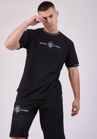 Camiseta negra de manga corta con cuello redondo y logo blanco, combinada con pantalones cortos negros que presentan una marca similar. Tejido suave de mezcla de algodón.