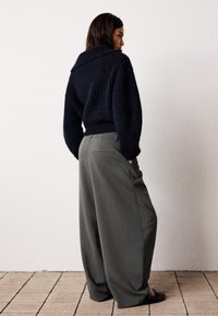 Dark navy knitted sweater with a wide collar, paired with loose, high-waisted grey trousers. The pants feature back pockets and a smooth texture.
